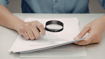 Image of person reviewing document with magnifying glass
